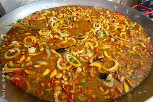 A vibrant seafood paella at a food festival, brimming with shrimp, calamari, and clams. The dish is colorful, with fresh ingredients. photo