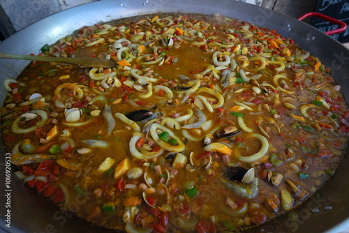 A vibrant seafood paella at a food festival, brimming with shrimp, calamari, and clams. The dish is colorful, with fresh ingredients. photo