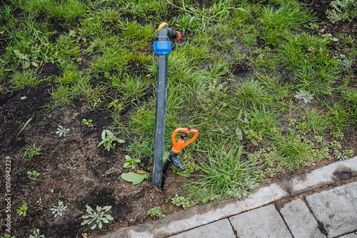 A green lawn with vibrant grass features a sprinkler positioned right next to a neatly laid brick walkway that provides a beautiful contrast to the surrounding landscape photo