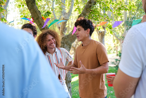 Obraz na płótnie Young man is gesturing with his hands while telling a story to his friends at an outdoor party w salonie