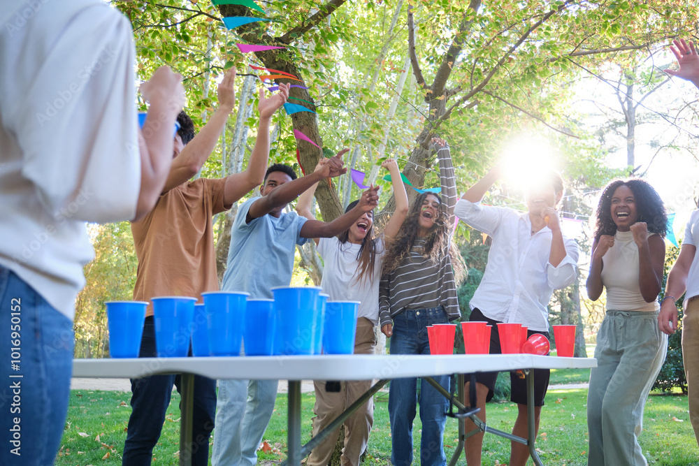 Group of friends is having a party in the park and celebrating winning a beer pong game