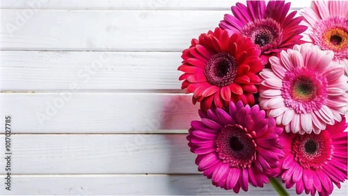 A top view of a bouquet of pink and red gerbera flowers on a white wooden table, with space for text.