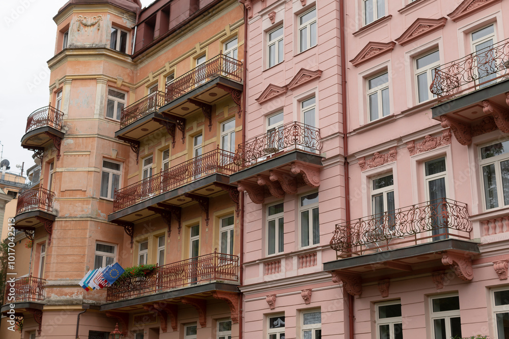 A charming row of pink buildings, each adorned with elegant balconies, which proudly display colorful flags fluttering gracefully from them A charming row of pink buildings, each adorned with elegant balconies, which proudly display colorful flags fluttering gracefully from them