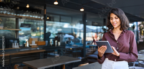 Young adult female entrepreneur owner of coffee shop or bar restaurant using tablet pc application for work. Indian or latin hispanic woman holding digital computer for business. Banner, copy space