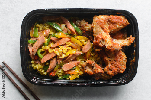 Overhead view of Singaporean noodles in a black disposable plate, top view of Singaporean fusion noodles with sliced peppers and sausage in a takeaway plate photo