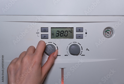 Woman's hand adjusting radiator temperature on a combi gas boiler. A close-up of a woman's hand with long nails turning the radiator temperature knob on the boiler's control panel. photo