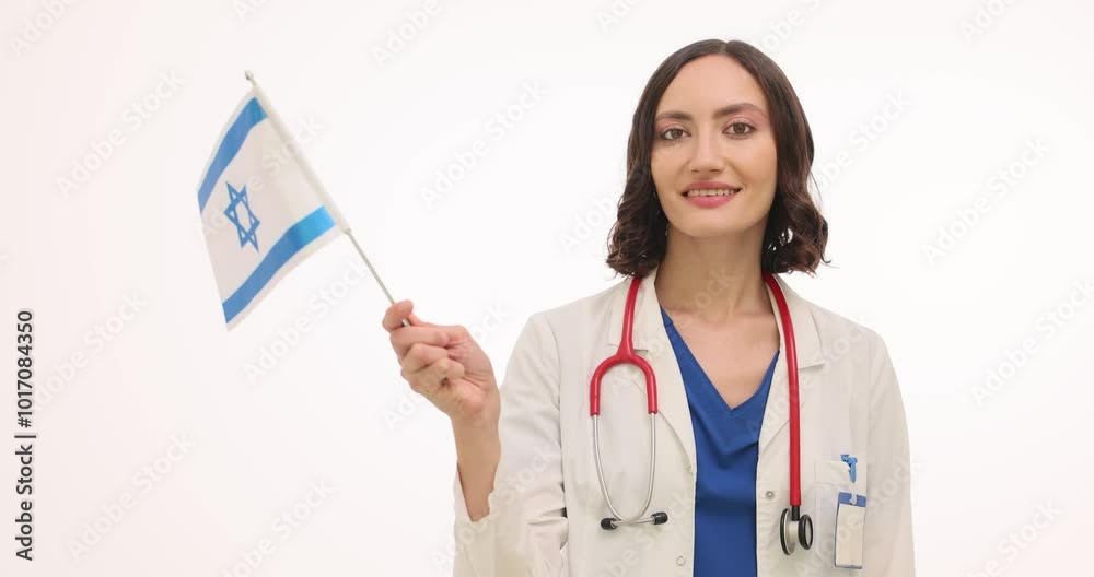 Woman doctor in uniform waves Israeli flag on white background. Smiling female medic with stethoscope welcomes medical staff from Israel Woman doctor in uniform waves Israeli flag on white background. Smiling female medic with stethoscope welcomes medical staff from Israel