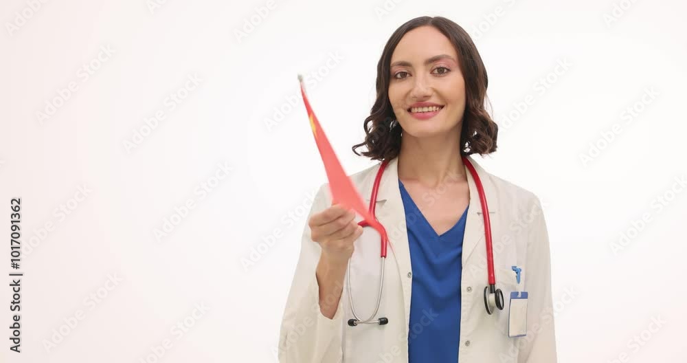 Smiling woman doctor waves small Chinese flag against white. Brunette female therapist with stethoscope greets co-workers from another country Smiling woman doctor waves small Chinese flag against white. Brunette female therapist with stethoscope greets co-workers from another country