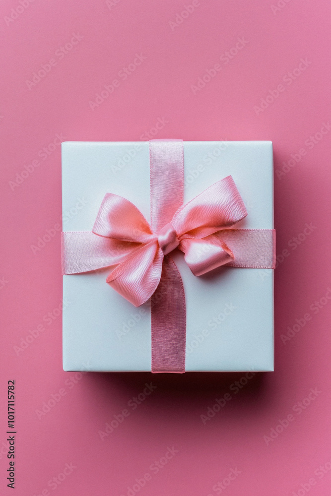 A white box with a pink ribbon on top. The ribbon is tied in a bow. The box is placed on a pink background A white box with a pink ribbon on top. The ribbon is tied in a bow. The box is placed on a pink background