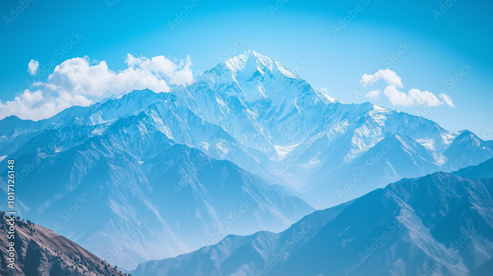 Fototapeta premium Snow-capped mountains under a clear blue sky with white clouds.