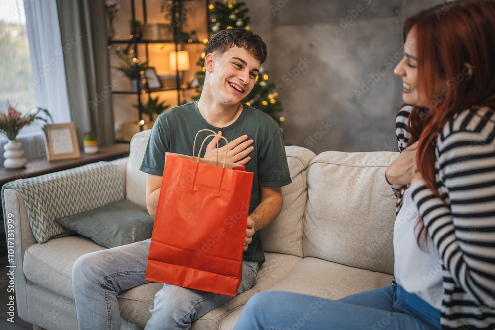 Obraz premium Girlfriend give christmas gift from shopping bag to boyfriend at home