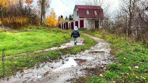 Little toddler child kid boy playing outside in boots in muddy puddle after rain in garden,home backyard at autumn.Carefree childhood.Moody fall weather forecast