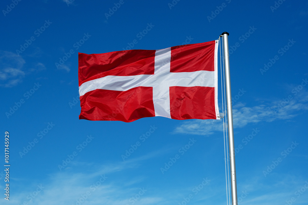 The flag of Denmark flutters in the wind against a blue cloudless sky The flag of Denmark flutters in the wind against a blue cloudless sky