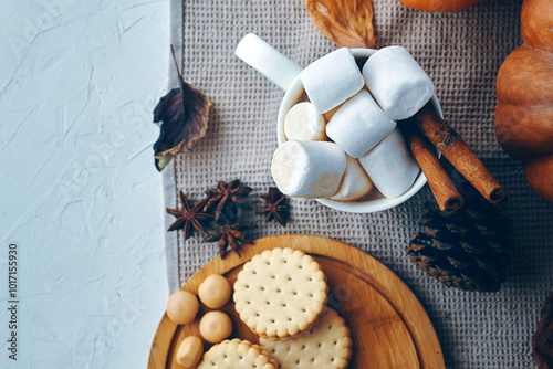 An overhead view shows a cozy arrangement featuring marshmallows, cookies, and fall spices on a rustic surface