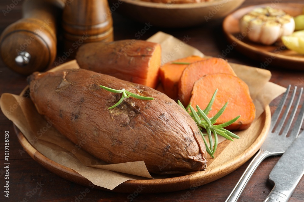 Tasty cooked sweet potatoes served with rosemary on wooden table, closeup Tasty cooked sweet potatoes served with rosemary on wooden table, closeup