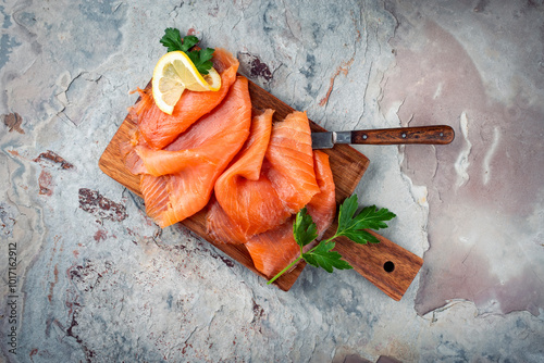Traditional Norwegian smoked salmon in slices with parsley and lemon served as top view on a rustic wooden chopping board with text space