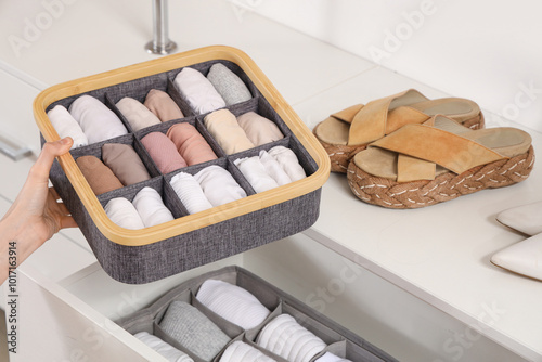 Beautiful young woman with clean clothes in organizers at wardrobe, closeup photo
