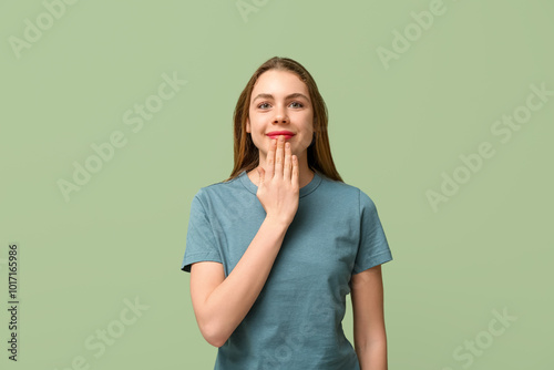 Young deaf mute woman using sign language on green background photo