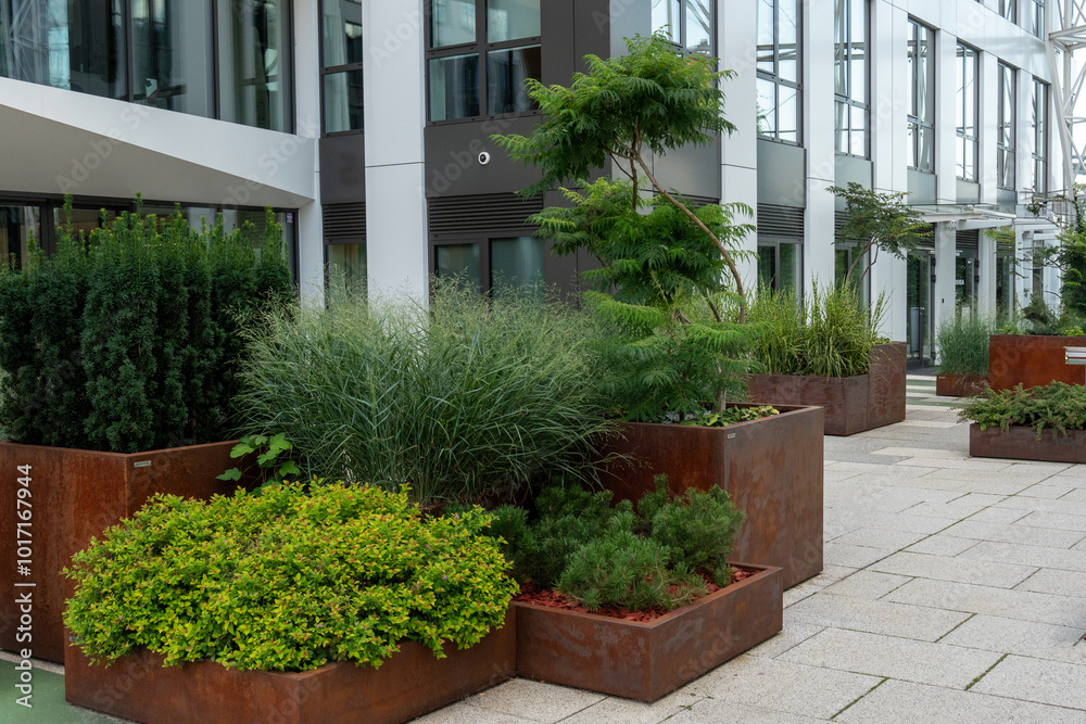 Fototapeta premium Contemporary office building features large, planters filled with lush greenery, creating a natural urban environment. Landscaping, beautiful flowerbeds in an urban environment. High quality photo