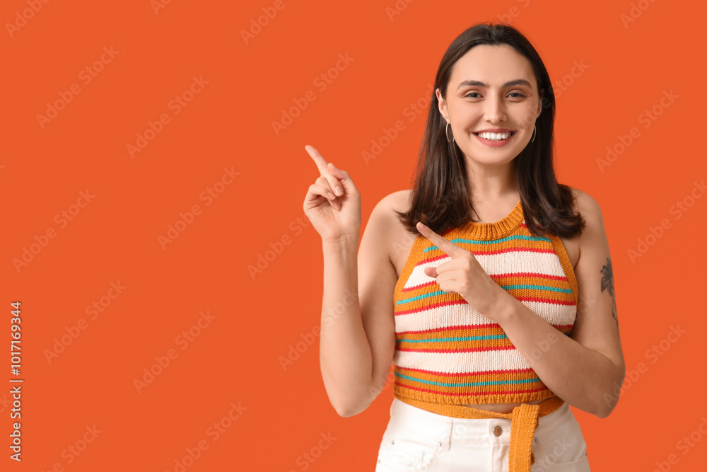Smiling young woman pointing at something on orange background Smiling young woman pointing at something on orange background