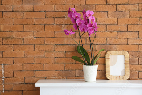 Orchid flower with frame on mantelpiece near brick wall