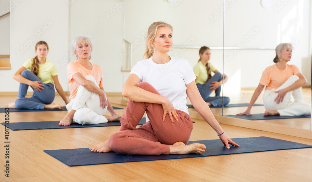 Fototapeta premium Sporty middle age european woman doing stretching workout during group training in yoga class