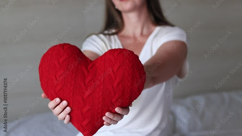 Girl holding knitted red heart, close-up. Valentine's Day. Heart-shaped pillow. Valentine's Day gift. Girl sitting on bed with toy heart. Symbol of love, gift. Romantic young woman with pillow Girl holding knitted red heart, close-up. Valentine's Day. Heart-shaped pillow. Valentine's Day gift. Girl sitting on bed with toy heart. Symbol of love, gift. Romantic young woman with pillow