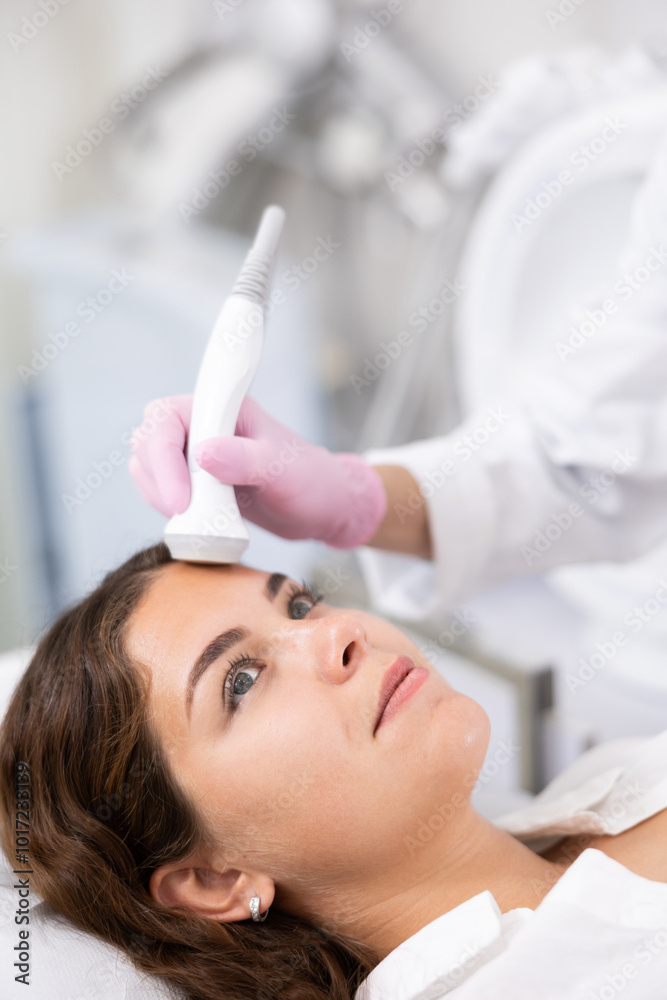 Naklejka premium Faceless cosmetologist doing facial skin ultrasound cavitation for flawless woman face laying in beauty salon indoors