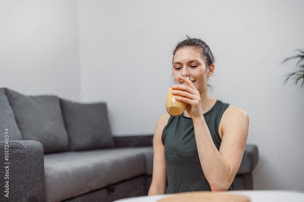 A young woman drinks a vegetable and fruit smoothie in her living room and doing yoga on yoga mat. A young woman drinks a vegetable and fruit smoothie in her living room and doing yoga on yoga mat.