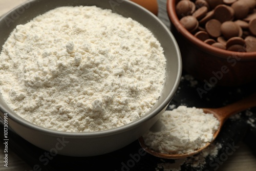 Flour in bowl and chocolate chips for making dough on table, closeup