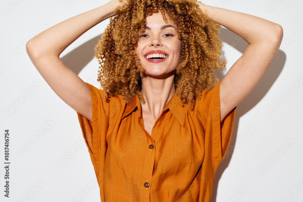 Smiling woman with curly hair wearing an orange shirt, joyful expression, hands on head, white background, showcasing happiness and positivity Her facial features highlight her vibrant personality Smiling woman with curly hair wearing an orange shirt, joyful expression, hands on head, white background, showcasing happiness and positivity Her facial features highlight her vibrant personality