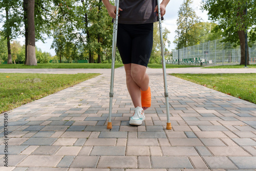 depersonalized young woman stands in summer park, leg in cast, leaning on crutches. photo