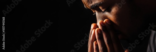 Close-up portrait of an African American man praying with his hands clasped together, his eyes closed in contemplation and devotion. This image captures the essence of faith, hope, and spirituality.