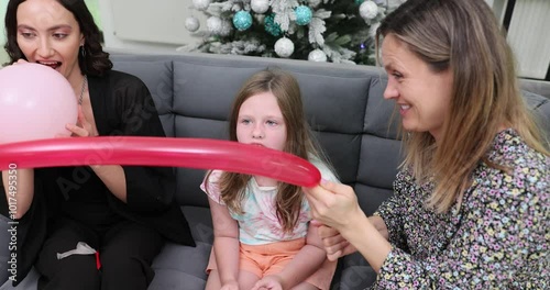 Happy women and girl child inflate various balloons preparing for party at home. Cheerful ladies engages in preparation for celebrating Christmas holiday slow motion