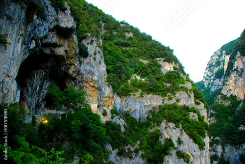 Curious scenery with the cave of Tempio del Valadier in Parco Naturale Gola della Rossa e di Frasassi, a wrinkly grotto with darker veinings stands as a shelter before the vertiginous gorge and peaks photo