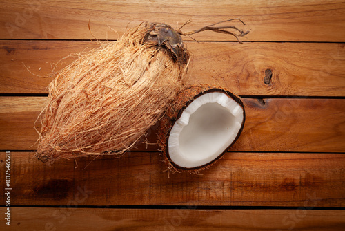 A close-up of a fresh whole coconut and a halved coconut on a wooden surface. photo