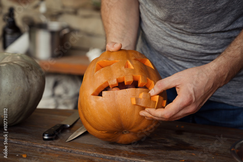 A close-up of hands carving a spooky Halloween pumpkin face on a wooden table using a knife. Celebrating the festive season with creative expression and craftsmanship.