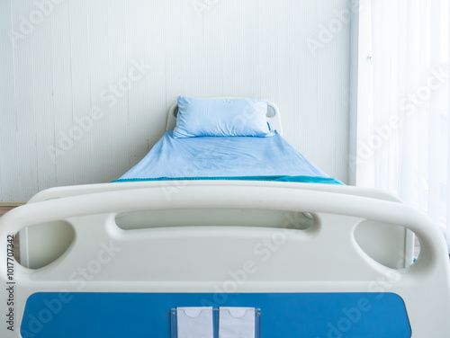 Front view of an empty hospital bed featuring blue bedding and a pillow, placed in a bright, minimalist admission room with soft natural lighting