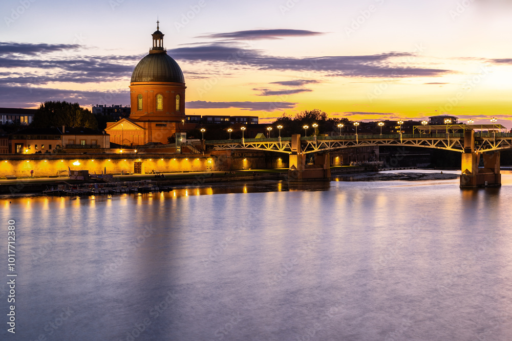 Fototapeta premium Golden sunset over Garonne river with views on the the pedestrian Saint-Pierre bridge, Place Saint-Pierre and the Grave hospital seen from the riverside 