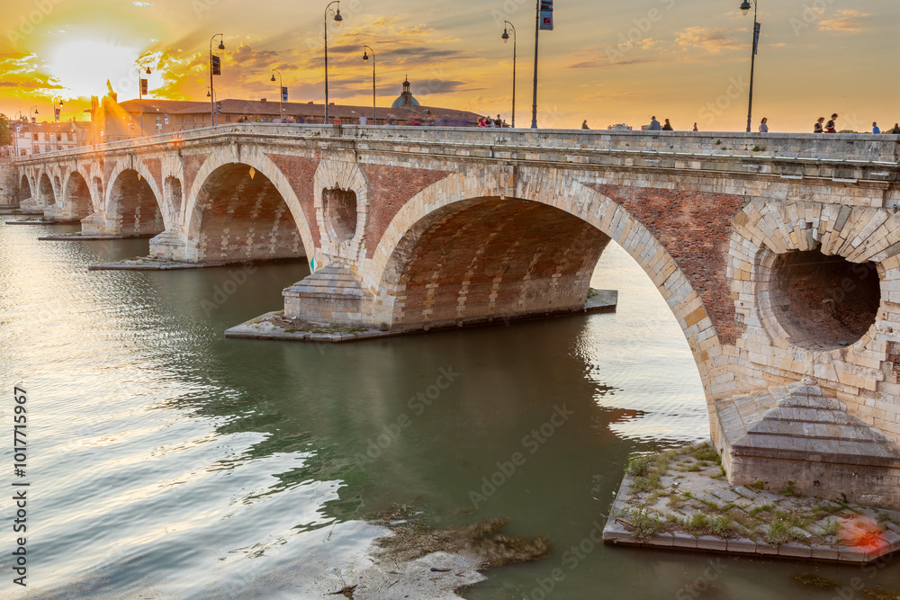 Obraz premium Golden sunset over the Garonne river and Pont Neuf in downtown Toulouse. This arch bridge is considered a masterpiece of the Renaissance. The bridge is not symmetrical.