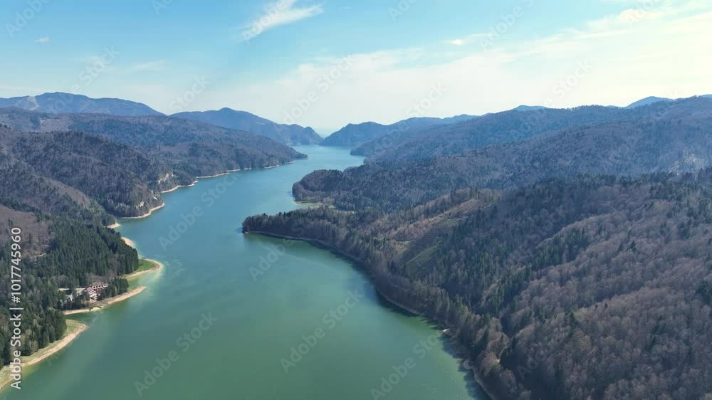 A peaceful river winding through forested mountains under a bright blue sky, aerial view
