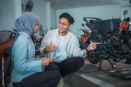 man with thumbs up and veiled saleswoman checking the underframe of a motorcycle at a showroom photo