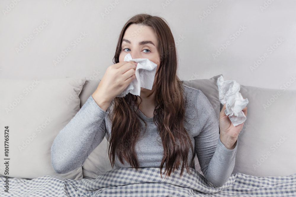 The brunette woman is sick, she has a runny nose and wipes her nose with napkins. Home interior The brunette woman is sick, she has a runny nose and wipes her nose with napkins. Home interior