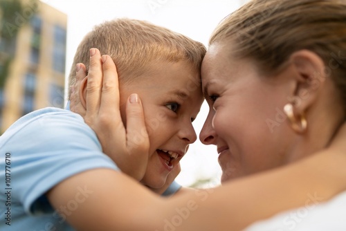 A joyful moment shared between a mother and her son outdoors, laughing and enjoying their time together in the afternoon sunlight