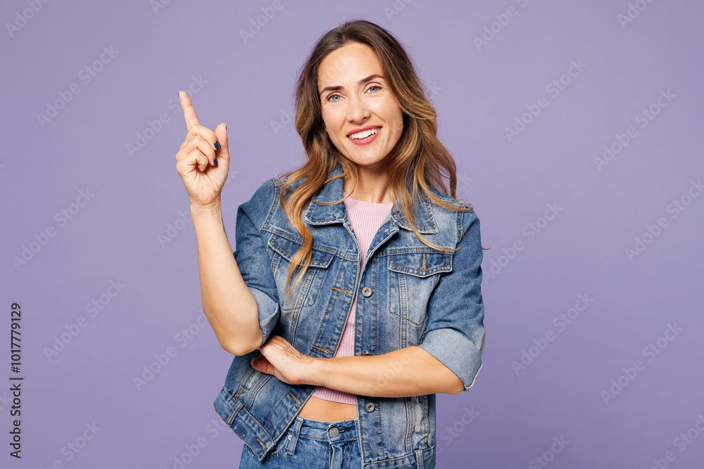 Young happy woman she wear denim jacket violet top casual clothes point index finger aside indicate on area mockup isolated on plain pastel light purple background studio portrait. Lifestyle concept. Young happy woman she wear denim jacket violet top casual clothes point index finger aside indicate on area mockup isolated on plain pastel light purple background studio portrait. Lifestyle concept.