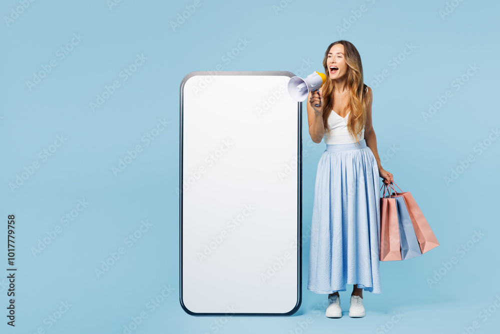 Full body young woman wear casual clothes hold shopping package bags big blank screen area mobile cell phone scream in megaphone isolated on plain blue background. Black Friday sale buy day concept. Full body young woman wear casual clothes hold shopping package bags big blank screen area mobile cell phone scream in megaphone isolated on plain blue background. Black Friday sale buy day concept.