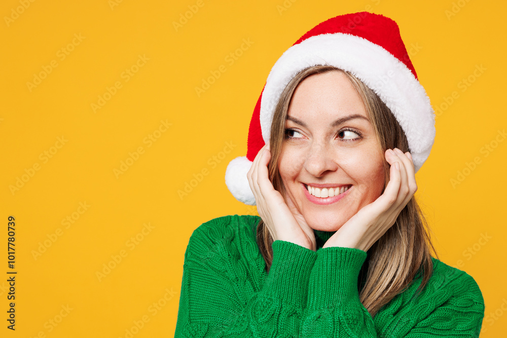 Close up merry young smiling woman wear green warm cozy sweater Santa hat posing put hands on face look aside isolated on plain yellow background. Happy New Year celebration Christmas holiday concept Close up merry young smiling woman wear green warm cozy sweater Santa hat posing put hands on face look aside isolated on plain yellow background. Happy New Year celebration Christmas holiday concept
