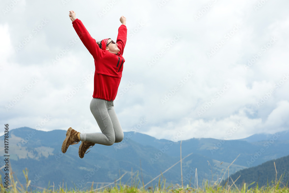 Happy young hiker jumping in mountains, low angle view. Space for text Happy young hiker jumping in mountains, low angle view. Space for text