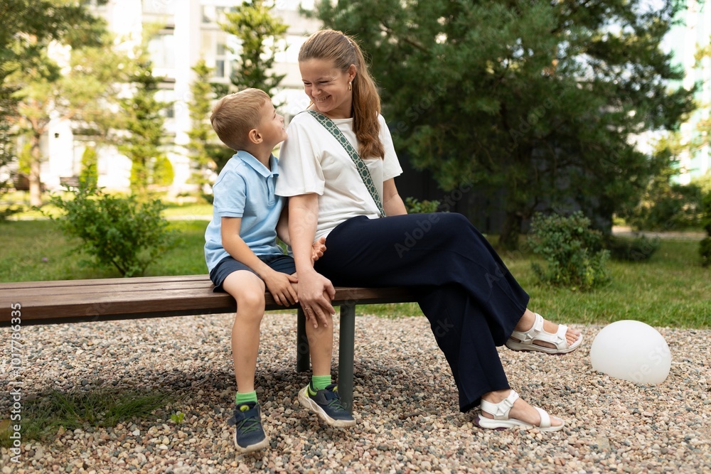 A joyful moment between a mother and her son sitting on a bench in a park, sharing smiles and laughter on a sunny afternoon A joyful moment between a mother and her son sitting on a bench in a park, sharing smiles and laughter on a sunny afternoon