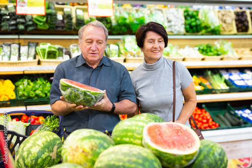 Mature woman and man selecting watermelon in greengrocer photo